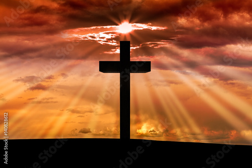 Jesus Christ wooden cross on a scene with dark red orange sunset, twilight light in the background, dramatic sky, clouds, sun rays, sunbeams. Christian Easter, resurrection,Good Friday concept 