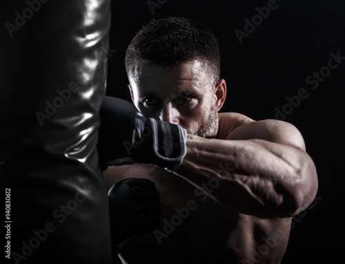 Studio shot of male boxer punching a boxing bag.