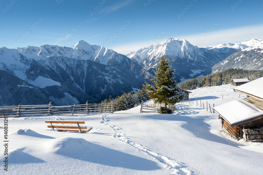 Winterlandschaft mit Schneespur und Almhütten in den Alpen