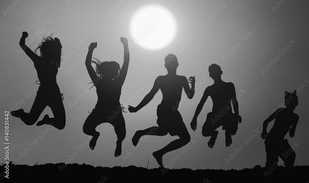 Obraz premium Silhouettes of five teenage boys and girls jumping in the air on the beach against sunset sky on beautiful summer day