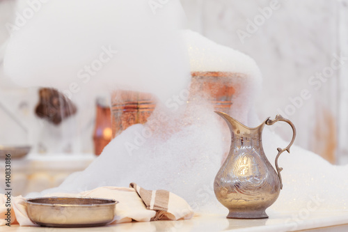 Making soap foam for massage. Water jar, towel and copper bowl with soap foam in turkish hamam. Traditional interior details