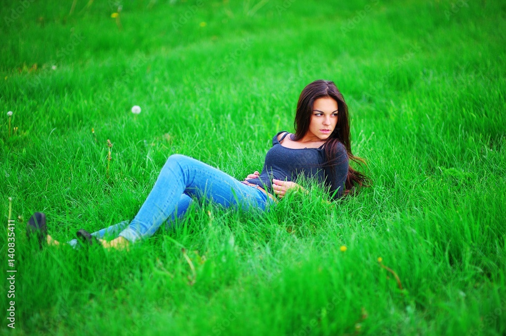 Wonderful portrait of a young handsome long-haired brunette woman lying on the lawn in bright green grass