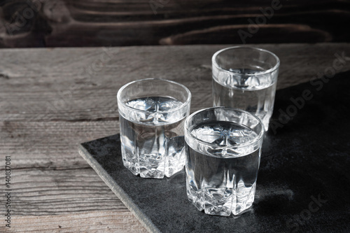 Vodka shots with ice cubes on black stone,