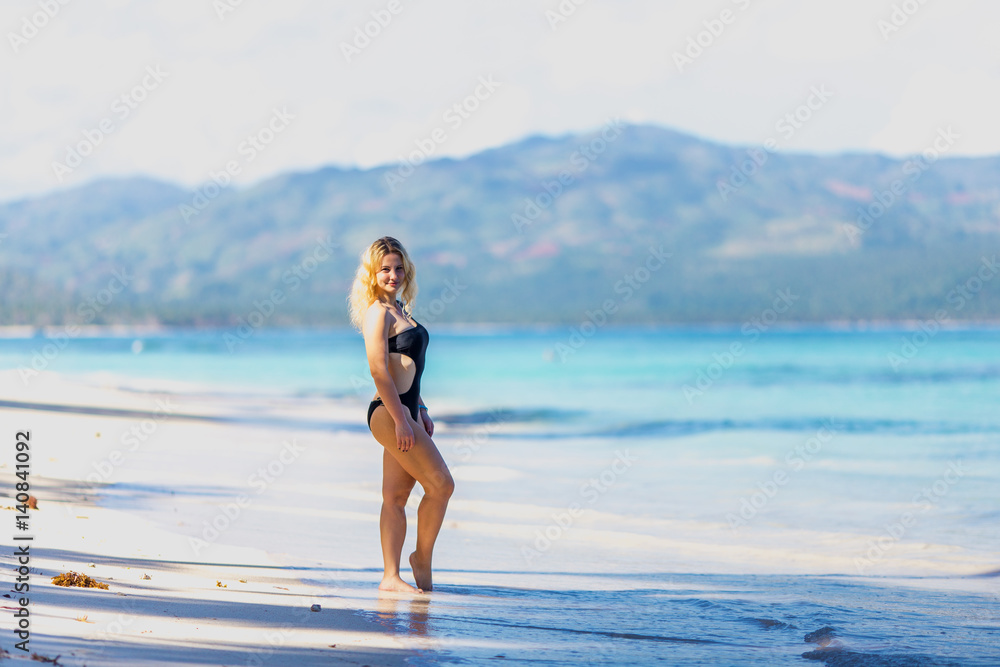 young beautiful girl in black swimwear in full growth on the blue beach