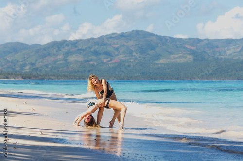 two pretty young girls in bikini exercising bridge pose yoga on the beach © Sergey