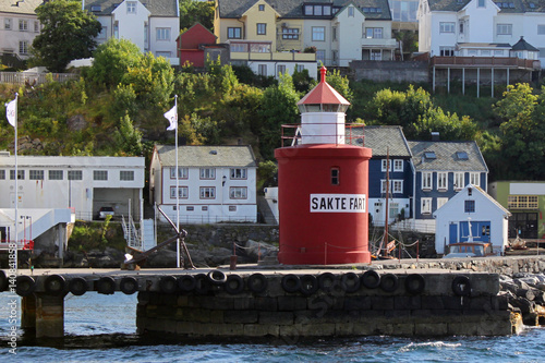 Gute Fahrt: Inschrift am Leuchtturm im Hafen der Stadt Alesund, Norwegen, mit Bootshaus und Wohnhäusern im Hintergrund