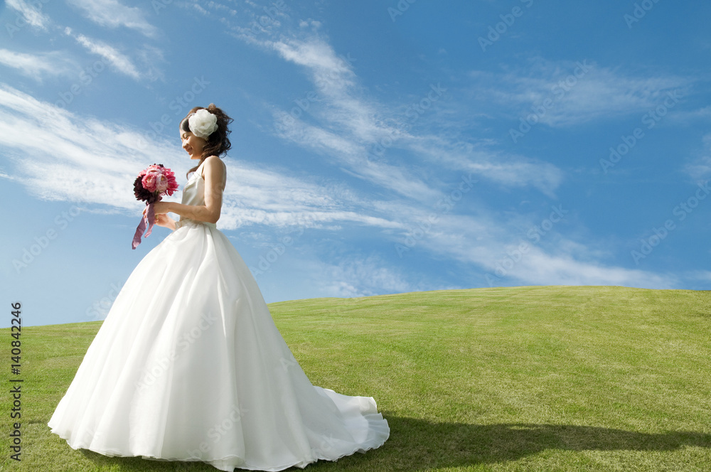 Bride in wedding dress holding flowers and standing against blue sky Bride in wedding dress holding flowers and standing against blue sky