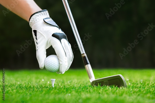 Hand putting golf ball on tee with club in golf course