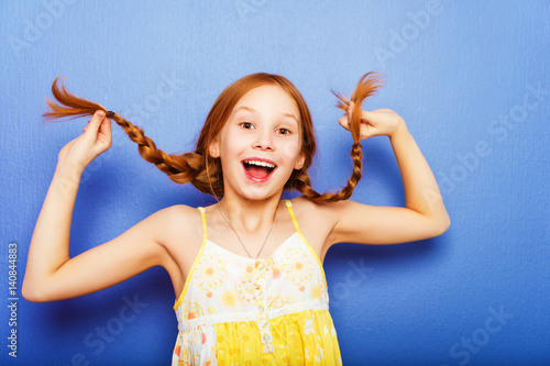 Studio shot of young preteen 9-10 year old redhead girl wearing yellow top, standing against blue purple background