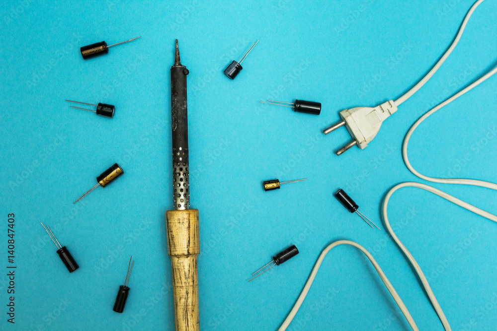 Old soldering iron and capacitors on a blue background.