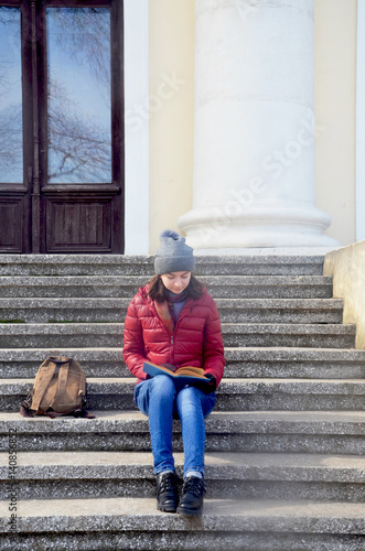 A beautiful young woman sitting on rhe stairs with a book