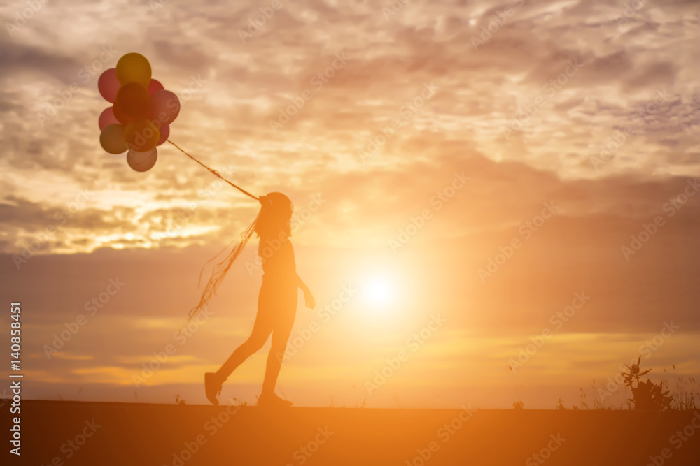 silhouette of young woman holding colorful of balloons with sunset