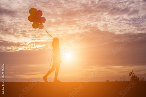 silhouette of young woman holding colorful of balloons with sunset