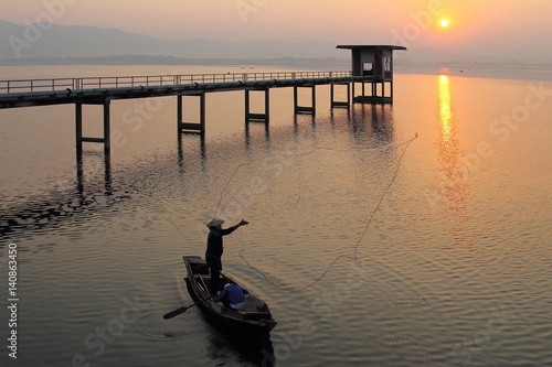Silhouette of fishermen using nets to catch fish at the Bangpra lake with beautiful scenery of nature during sunrise time. Bang Pra Reservoir at Chonburi province in Thailand