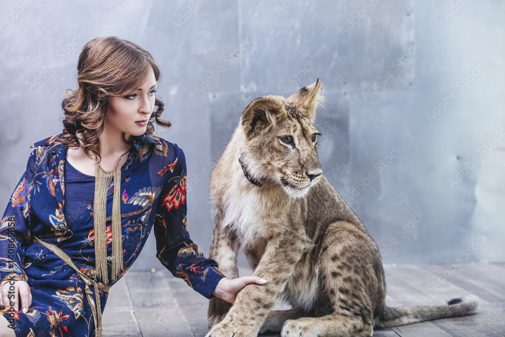 Obraz premium Beautiful fashionable young woman with a little alive lion cub