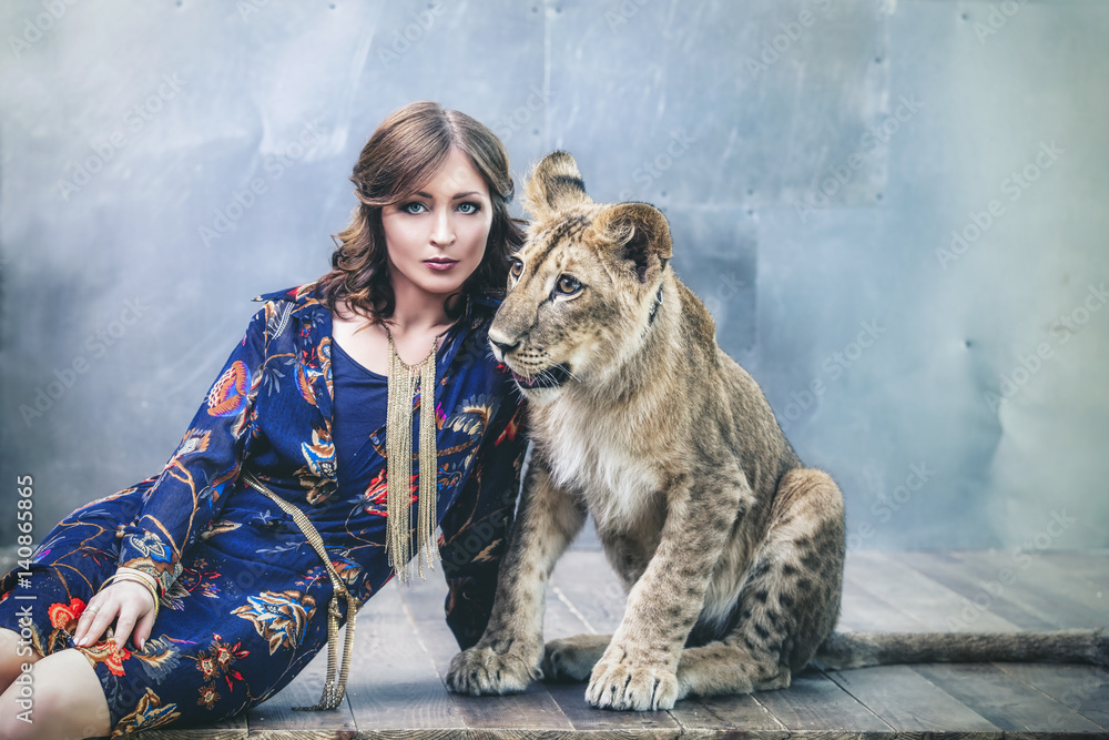 Obraz premium Beautiful fashionable young woman with a little alive lion cub