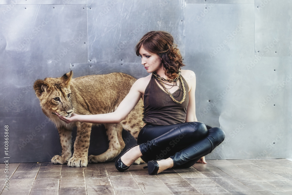Obraz premium Beautiful fashionable young woman with a little alive lion cub