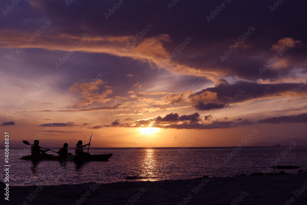 Silhouette family kayaking on the beach with sunset background in Thailand. 