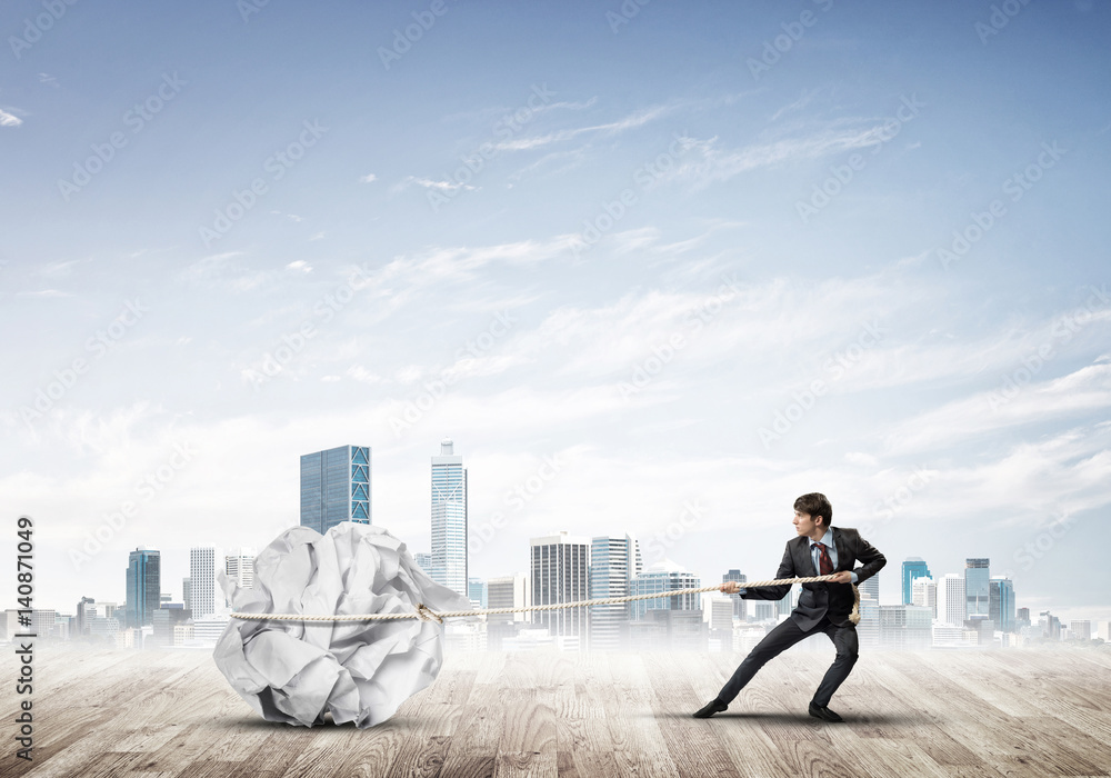 Man pulling with effort big crumpled ball of paper as creativity sign Man pulling with effort big crumpled ball of paper as creativity sign