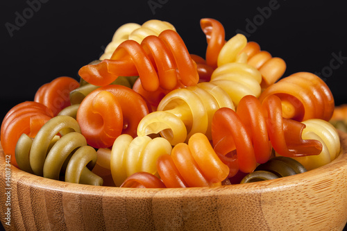 Spiral pasta trottole tricolore isolated in wooden bowl  on black background photo