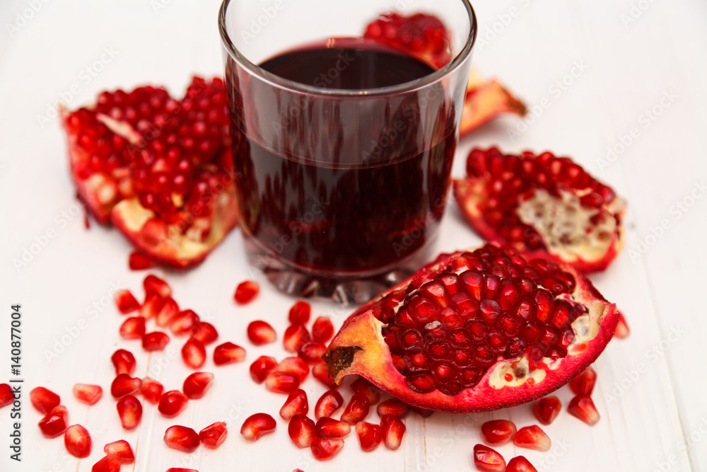 A glass of pomegranate juice and a pomegranate grain on a white wooden background A glass of pomegranate juice and a pomegranate grain on a white wooden background