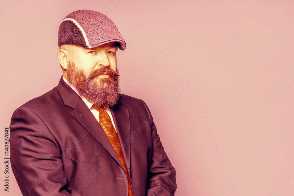 Adult bearded man in a suit and cap on a pink background Adult bearded man in a suit and cap on a pink background