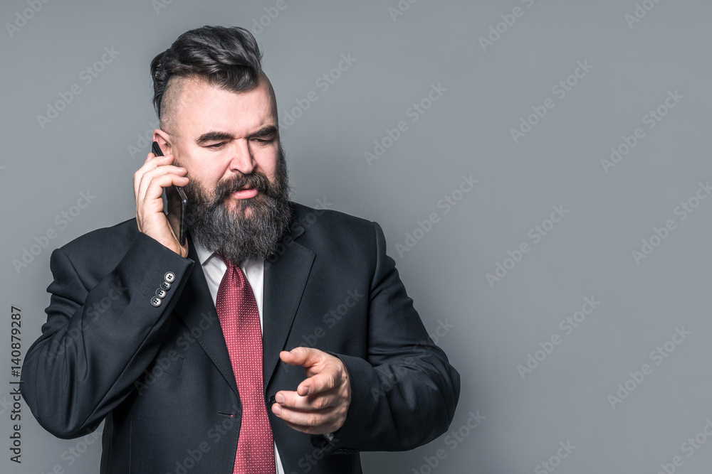 Adult bearded man in a suit holding a phone on a gray background Adult bearded man in a suit holding a phone on a gray background