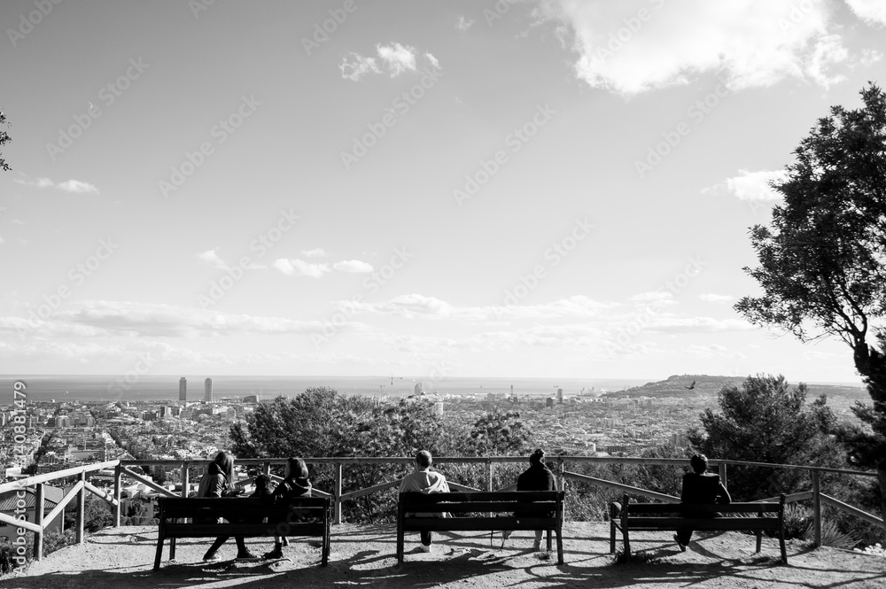 people sit on bench in outdoor park watching barcelona landscape