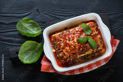 Lasagna bolognese over black wooden background, top view, studio shot