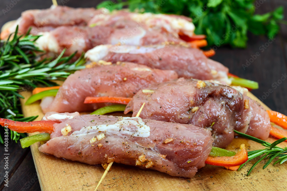 Un-cooked, pork meat rolls stuffed with vegetables (pepper, carrots) in hot garlic sauce on a cutting board. Raw, semi-finished product. Un-cooked, pork meat rolls stuffed with vegetables (pepper, carrots) in hot garlic sauce on a cutting board. Raw, semi-finished product.