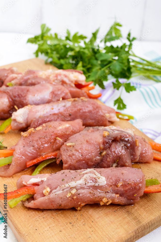 Un-cooked, pork meat rolls stuffed with vegetables (pepper, carrots) in hot garlic sauce on a cutting board. Raw, semi-finished product. Un-cooked, pork meat rolls stuffed with vegetables (pepper, carrots) in hot garlic sauce on a cutting board. Raw, semi-finished product.