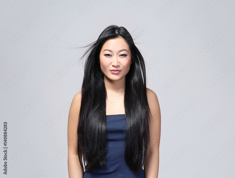 Beautiful Asian woman with long straight hair on light background