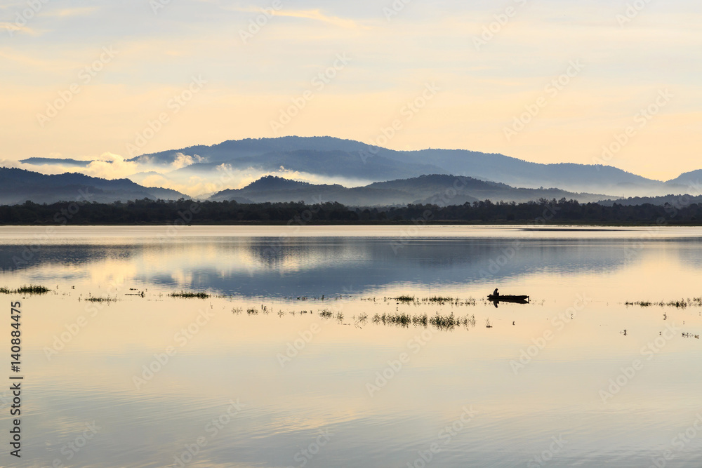 small fishing boat in lake with foggy over mountain background and reflection in the pond
