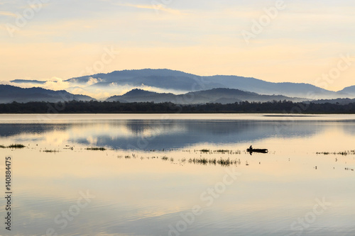 small fishing boat in lake with foggy over mountain background and reflection in the pond 