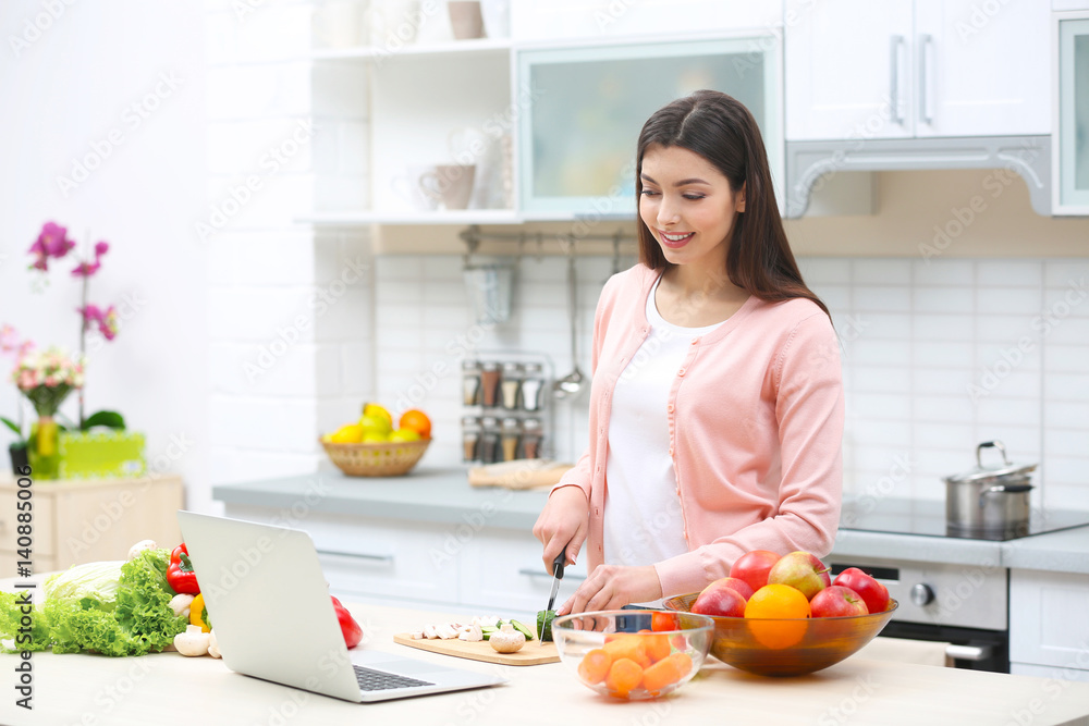 Beautiful young woman cutting products in kitchen