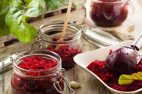 Grated beetroot marinated in jars. Wooden background.