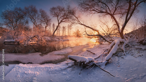 Beautiful calm evening on the small winter river, surrounded by overhanging trees. The last rays of the winter sun on the small forest river. Belarus, Minsk region