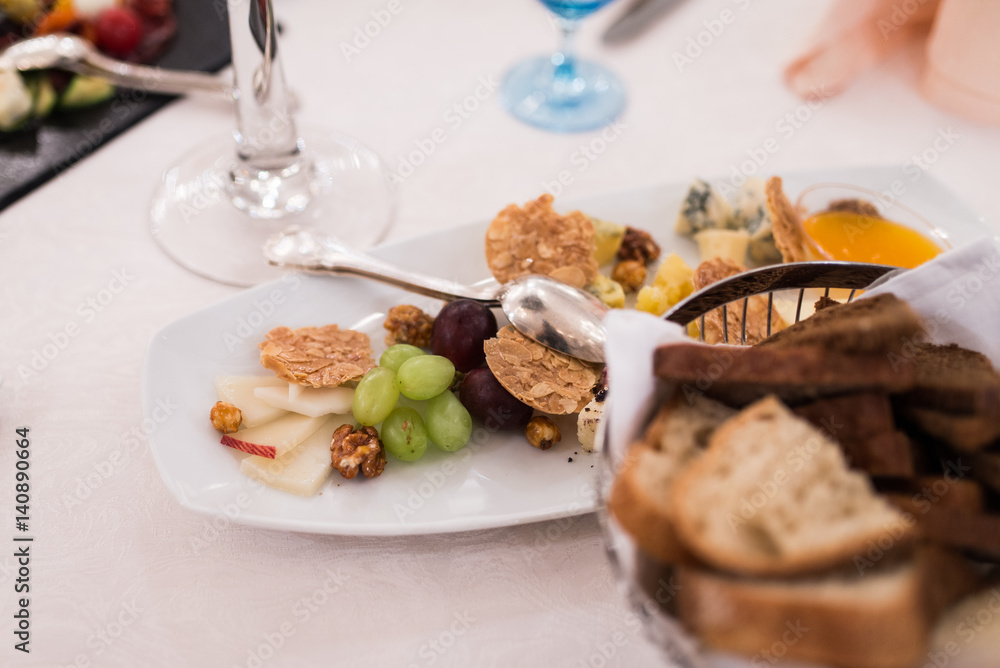 Appetizing food into the white plate on a banquet table: grape, cheese, nuts, snacks.