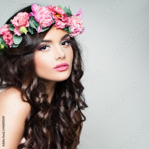 Perfect Brunette Model with Curly Hair and Flowers Wreath. Beautiful Woman with Makeup and Permed Hairstyle