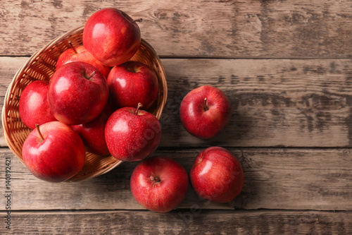 Wicker basket with fresh red apples on wooden background