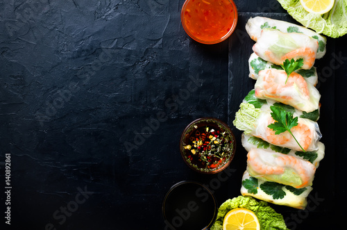Fresh Vietnamese, Asian, Chinese food frame on black concrete background. Spring rolls rice paper, lettuce, salad, vermicelli, noodles, shrimps, fish sauce, sweet chili, soy, lemon. Top view. photo