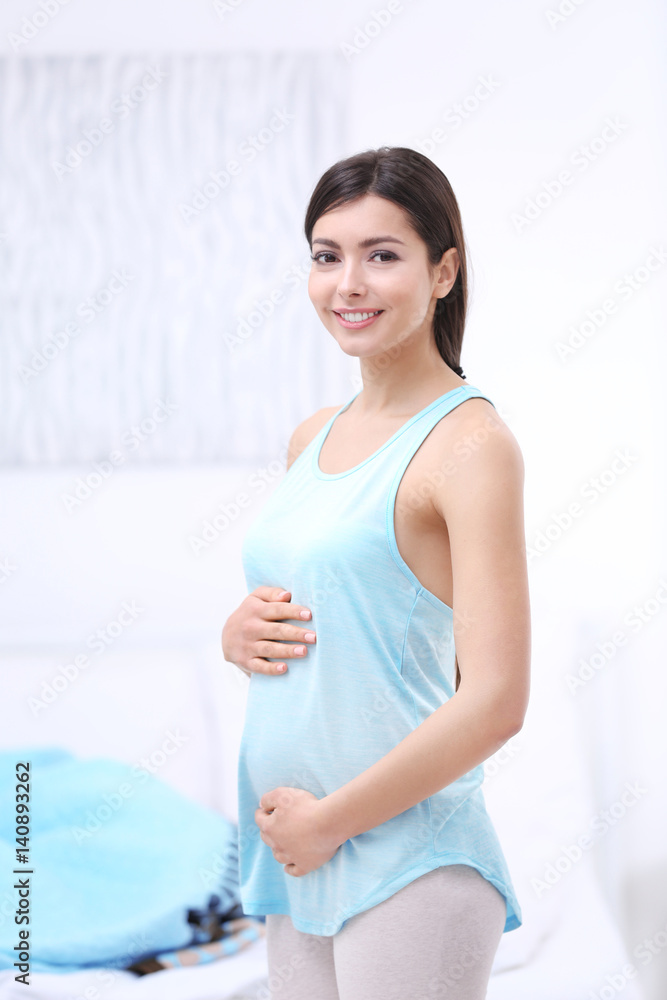 Portrait of beautiful happy pregnant woman touching her belly standing in light room