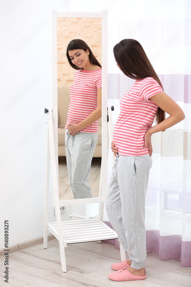 Beautiful pregnant woman looking in mirror in light room Beautiful pregnant woman looking in mirror in light room