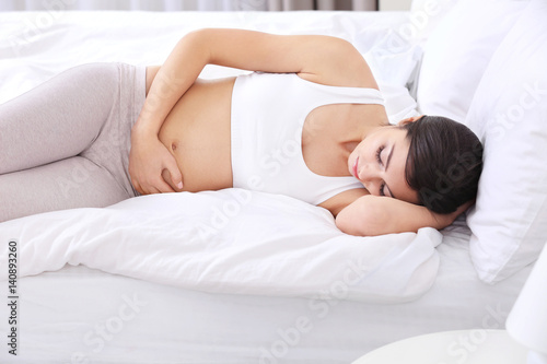 Beautiful pregnant woman touching her belly lying on bed at home © Africa Studio