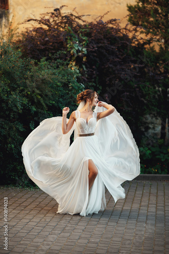 Pretty blonde bride dances in her summer gown before green bushes
