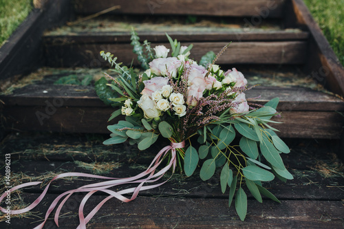 wedding bouquet of flowers and greenery is on the old wooden stairs in the forest