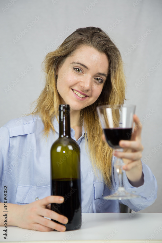 Young Caucasian white woman sitting at a table while drinking wine. She is blonde and pretty with light brown eyes. The background of the image is white. Young Caucasian white woman sitting at a table while drinking wine. She is blonde and pretty with light brown eyes. The background of the image is white.