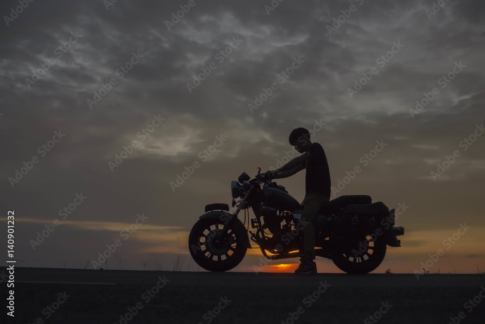 Fototapeta premium Silhouette biker with his motorbike beside the natural lake and beautiful sunset sky.