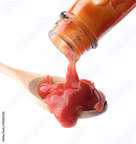 Tomato ketchup falling from bottle into spoon on white background