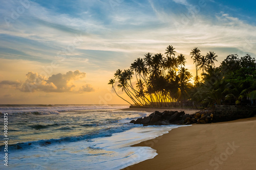 Fototapeta Naklejka Na Ścianę i Meble -  Beautiful tropical sunset with palm trees. Wijaya beach, Sri Lanka.